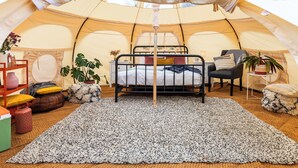 Een gezellige tent met een stapelbed, een klein tafeltje, stoelen en plantenpotten.
