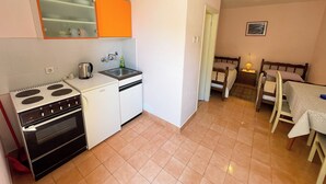 A compact kitchen with a stove, sink, and orange cabinets. There is a dining area with a table and chairs. - Studio apartment Šarić 3 (Kraljevica)