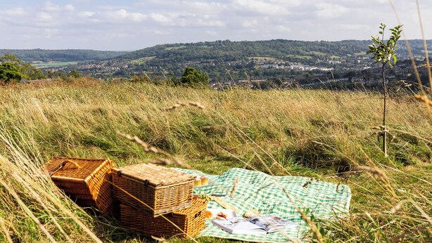 Picknickdecke mit Korb auf einem grasbewachsen Hügel mit Blick auf eine Stadt.