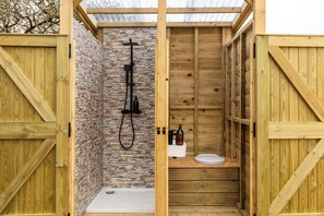 A wooden shower stall with a stone wall, a white sink, and a wooden bench. - Glamping - The Natterjack, Bath (Charlcombe)