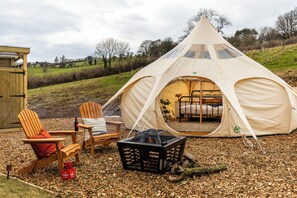 Een tent met een bed, twee houten stoelen, een tafel en een kist.