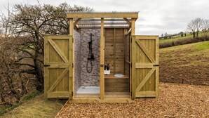Een houten douchecabine buiten, met een stenen muur, een wastafel en een toilet.