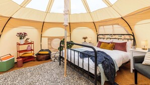 Een tent met een bed, nachtkastje, lamp en een klein plankje met decoratieve spullen.