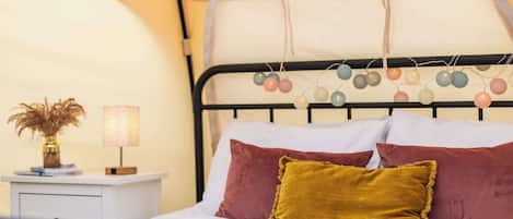 Un letto con una testiera decorata da ornamenti colorati pendenti, un comodino con una lampada e un vaso con fiori secchi.