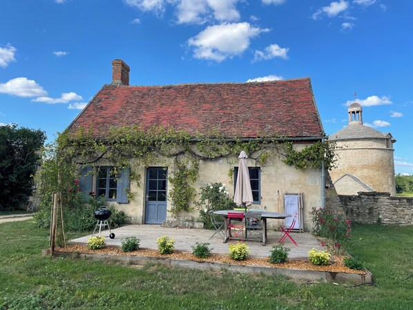 A rustic house with a red-tiled roof, ivy-covered walls, and a small garden with a table and chairs. - Gite du vigneron, Château de Meauce (Saincaize-Meauce)