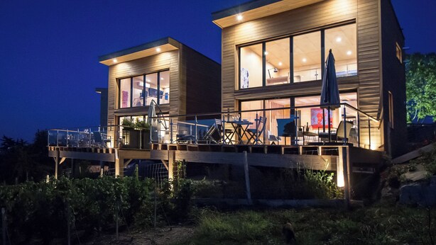 Une maison moderne à deux étages, dotée de grandes fenêtres, d’une terrasse et d’un espace salon extérieur.