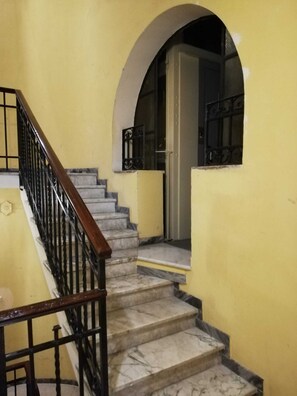 A staircase with marble steps and a wooden handrail, leading to a door with a metal gate.