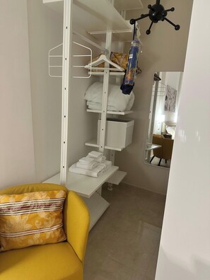 Habitación pequeña con cama, armario blanco, una mesita con toallas y una silla amarilla.