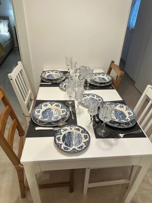 Una mesa de comedor dispuesta con platos azules y blancos, vasos de vidrio transparente y un mantel blanco.