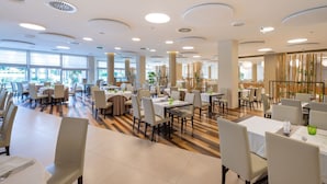 A spacious dining area with multiple tables and chairs, large windows, and a modern ceiling design. - Peaceful stay with spa near the marina (Bibione)