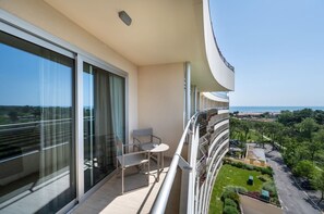 Un balcon avec une table et des chaises, de grandes fenêtres et une vue sur la mer et la verdure.