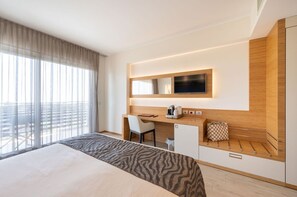 Ein Hotelzimmer mit einem großen Bett, einem Schreibtisch mit Stuhl, einem Fernseher und einer Minibar.
