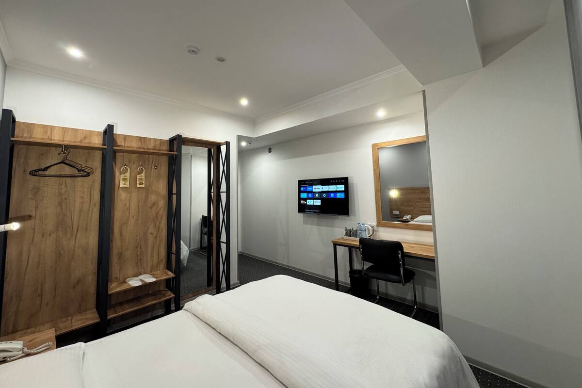 Una habitación de hotel con cama, escritorio, silla, televisor, armario y espejo.