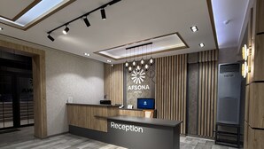 A hotel reception area with a modern design, featuring a reception desk labeled "Reception," a large wall-mounted sign for the hotel, and a wooden floor. - Afsona hotel (Qarshi)