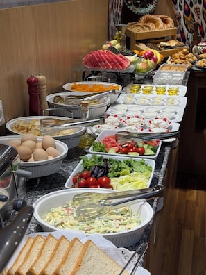 A buffet with various food items including fruits, vegetables, bread, and eggs. - Afsona hotel (Qarshi)
