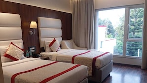 A hotel room with two beds, a large window, and a view of trees. - SS LUMINA HOTEL (Bengaluru)