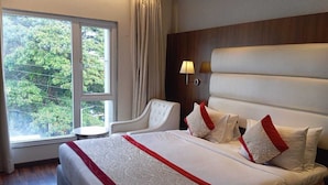 A hotel room with a large bed, a chair, a window with curtains, and a wall-mounted lamp. - SS LUMINA HOTEL (Bengaluru)