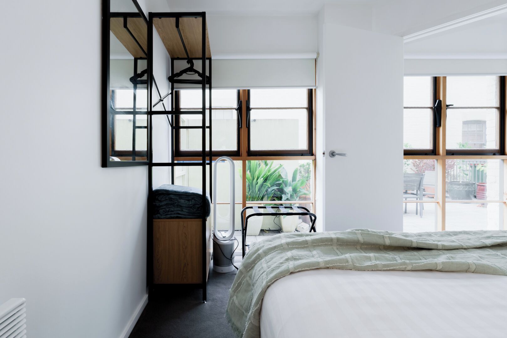 A bedroom with a bed, a wooden dresser, a mirror, and a window.