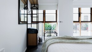 A bedroom with a bed, a wooden dresser, a mirror, and a window. - Cameron Mews: In The Heart Of The City (Launceston City)