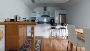 A modern kitchen with white cabinets, a wooden counter, and a dining area with white chairs. - Cameron Mews: In The Heart Of The City (Launceston City)