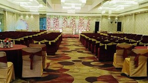 A large hall with rows of chairs and tables, a stage with floral decorations, and a patterned carpet. - Blessings Imperia (Prayagraj)