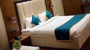 A bedroom with a large bed, wooden headboard, and a nightstand with a phone and a vase of flowers. - Blessings Imperia (Prayagraj)