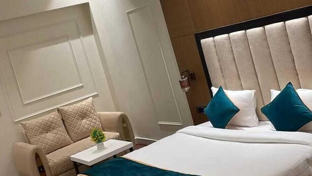 A modern hotel room with a large bed, a sofa, a small table, and a decorative plant. - Blessings Imperia (Prayagraj)
