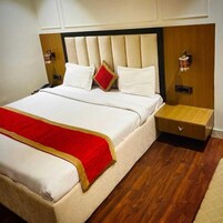 Una cama bien hecha con sábanas blancas y un edredón rojo, flanqueada por mesitas de noche de madera con lámparas, en una habitación con suelo de madera y cabecera color crema.