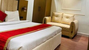 A hotel room with a large bed, a wardrobe, a seating area, and a wall-mounted light fixture. - Blessings Imperia (Prayagraj)