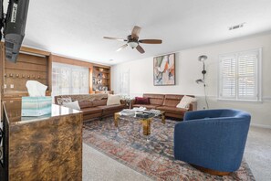 A living room with a brown sofa, a blue armchair, a coffee table, a ceiling fan, and a bookshelf.