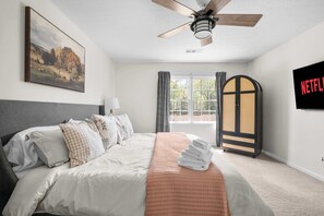 A bedroom with a bed, a ceiling fan, a painting, a wardrobe, and a TV screen displaying 'NETFLIX'.