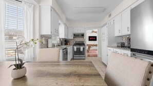A modern kitchen with white cabinets, a dining table, and a TV displaying 'NETFLIX.' - Serene Pool retreat w/ Games Near Fort Moore (Columbus)