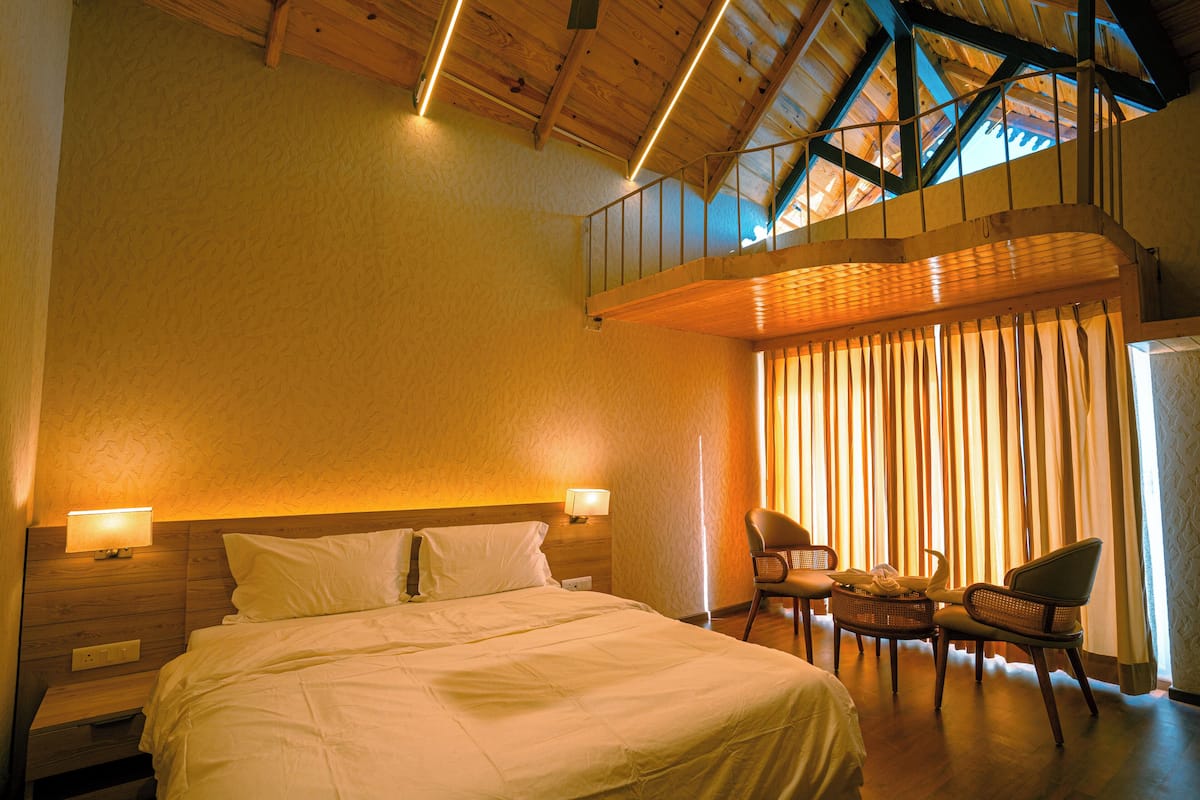 A hotel room with a large bed, two bedside tables, a chair, a small table, and a balcony with a view.
