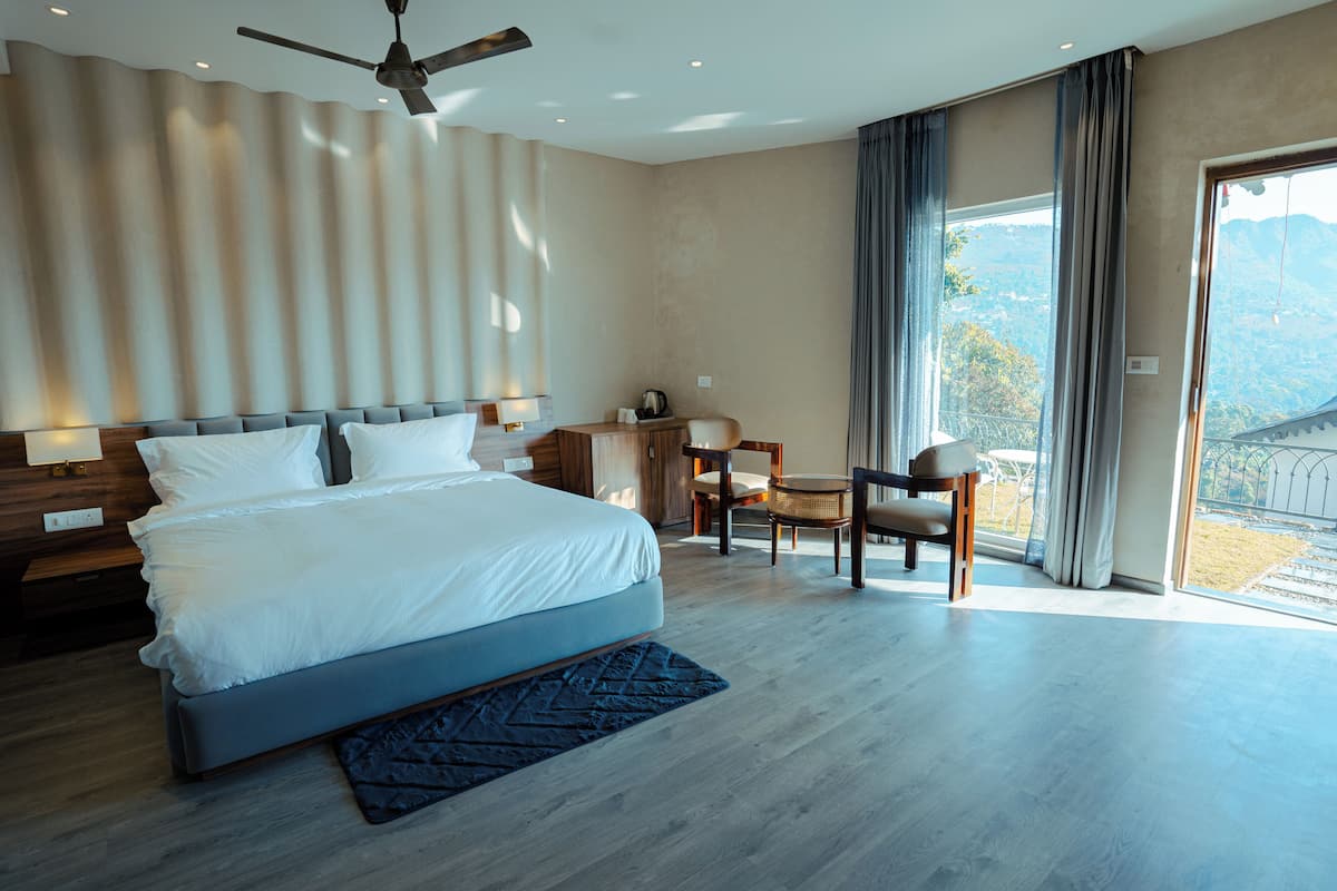 A modern hotel room with a large bed, a desk, and a view of the mountains.