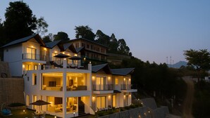 A multi-story house with a balcony, outdoor seating, and a well-lit interior. - The Barns Resorts (Bhimtal)