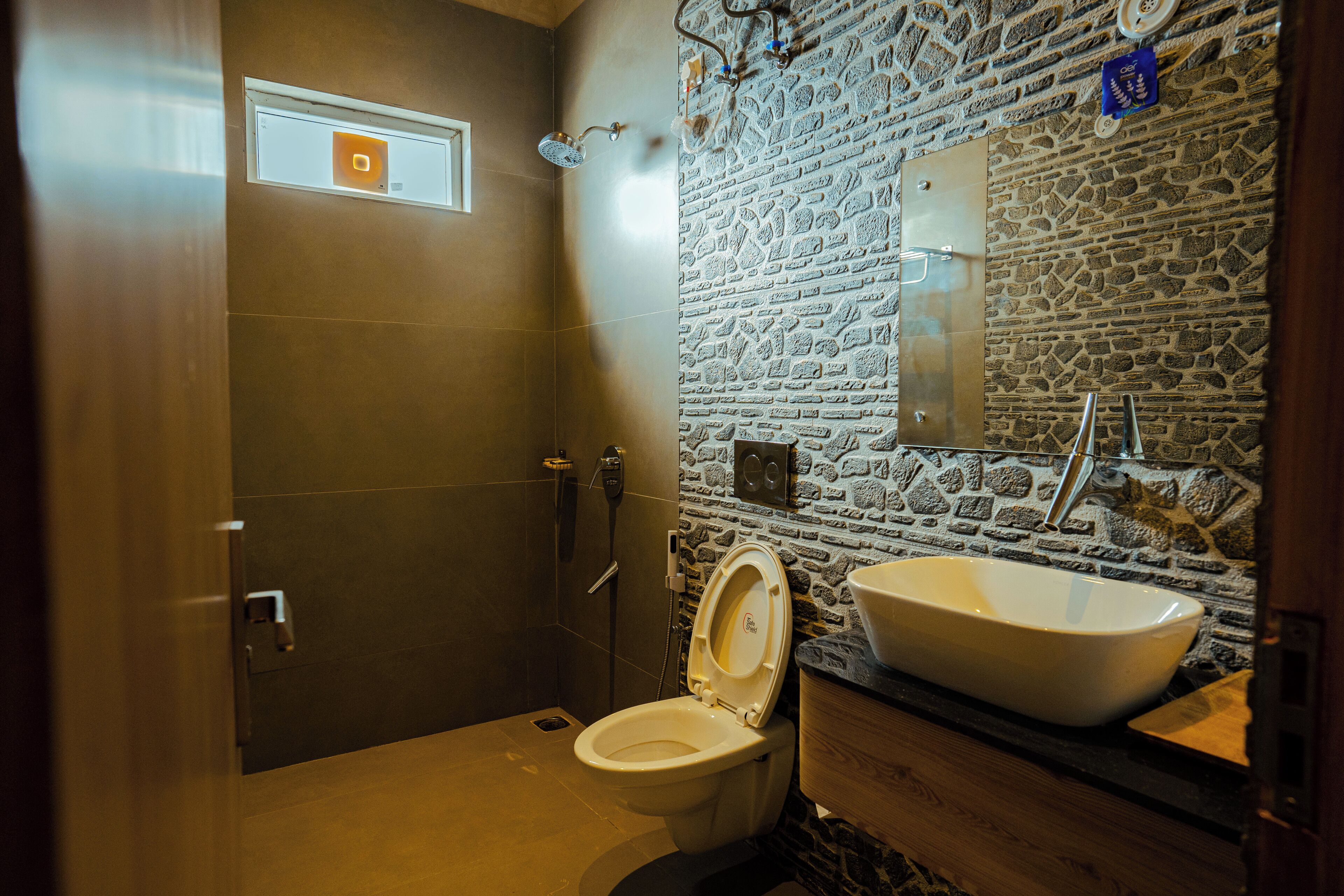Un baño con pared de piedra, un lavamanos blanco y un inodoro.