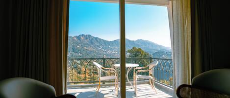A balcony with two wicker chairs and a small table, overlooking a mountainous landscape.