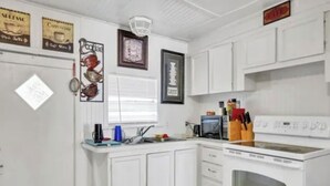 Una cocina con armarios blancos, una estufa y diversos utensilios.