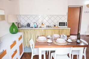 Uma sala de jantar com mesa posta para quatro pessoas, micro-ondas e pia ao fundo.