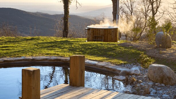 A wooden deck by a pond with a sauna and a stone structure in the background. - Between the mountains and the sea, a profound and eco-chic nature experience in (Montbolo)