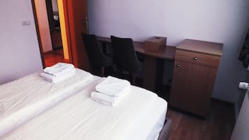 A hotel room with a bed, a desk, two chairs, and a small wooden cabinet.