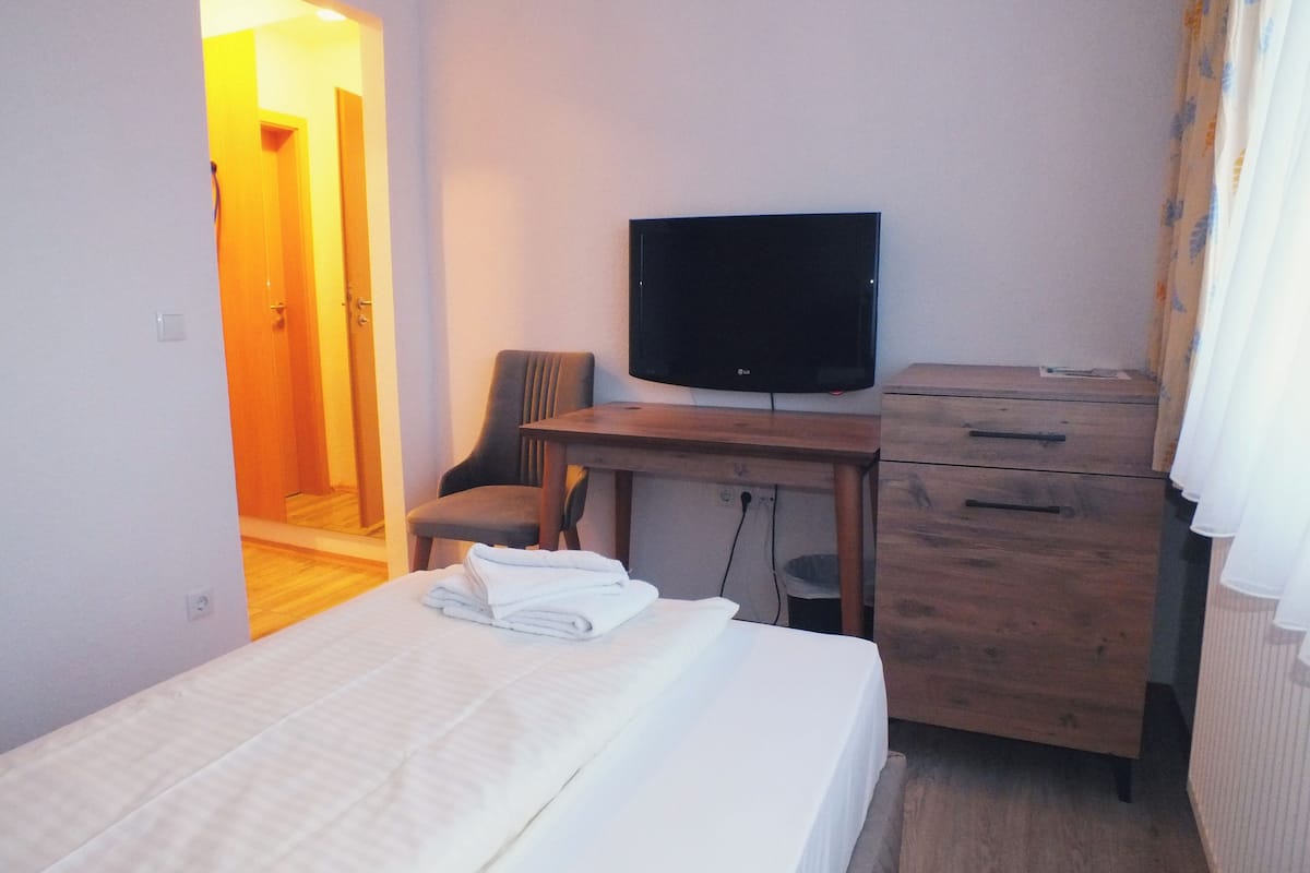 Een hotelkamer met een bed, een bureau met een televisie, een stoel en een houten dressoir.