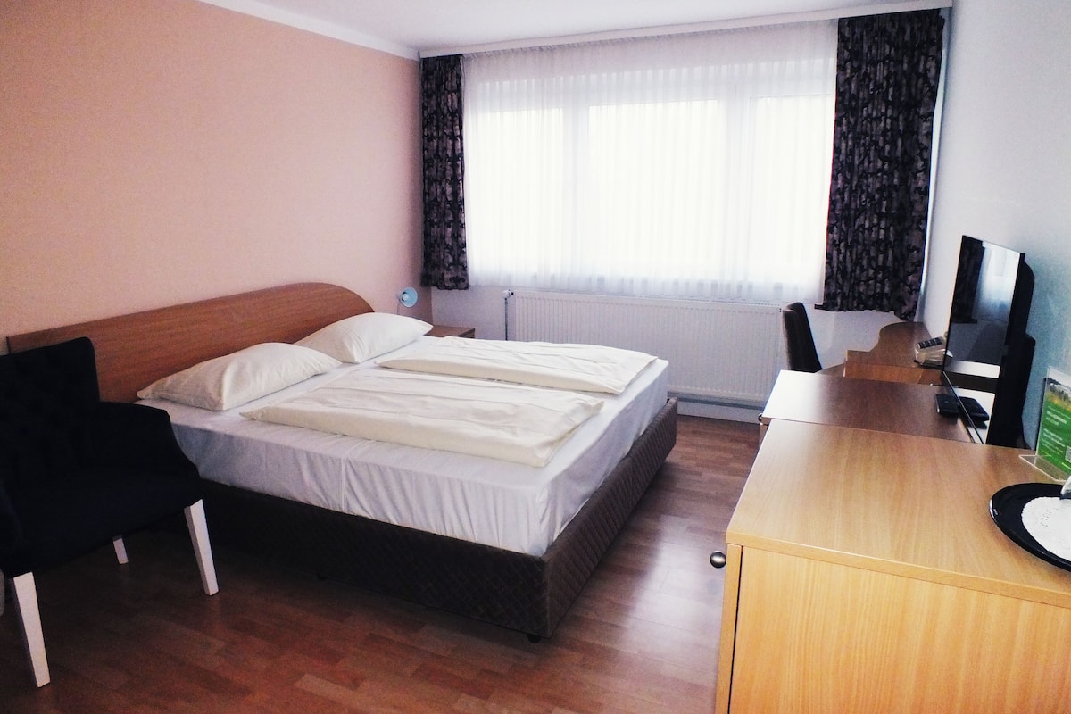 Een hotelkamer met een tweepersoonsbed, een houten bureau, een stoel, een televisie en een raam met gordijnen.