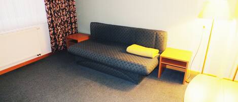 Une petite pièce accueillante, avec un canapé gris, un coussin jaune, une table d’appoint en bois et une lampe.