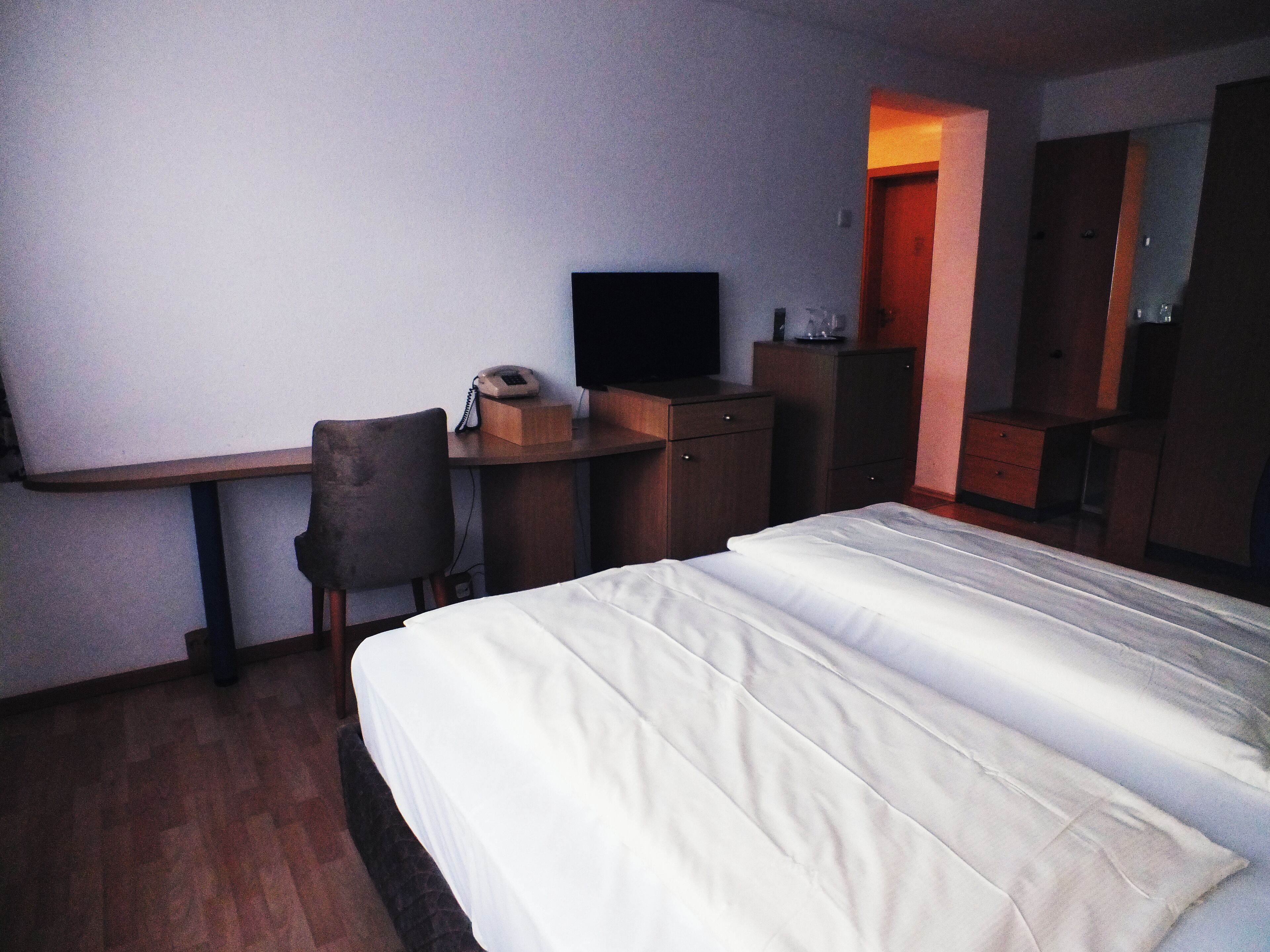 Ein Hotelzimmer mit Bett, Schreibtisch, Sessel, Fernseher und Kleiderschrank.