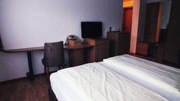 Ein Hotelzimmer mit Bett, Schreibtisch, Sessel, Fernseher und Kleiderschrank.