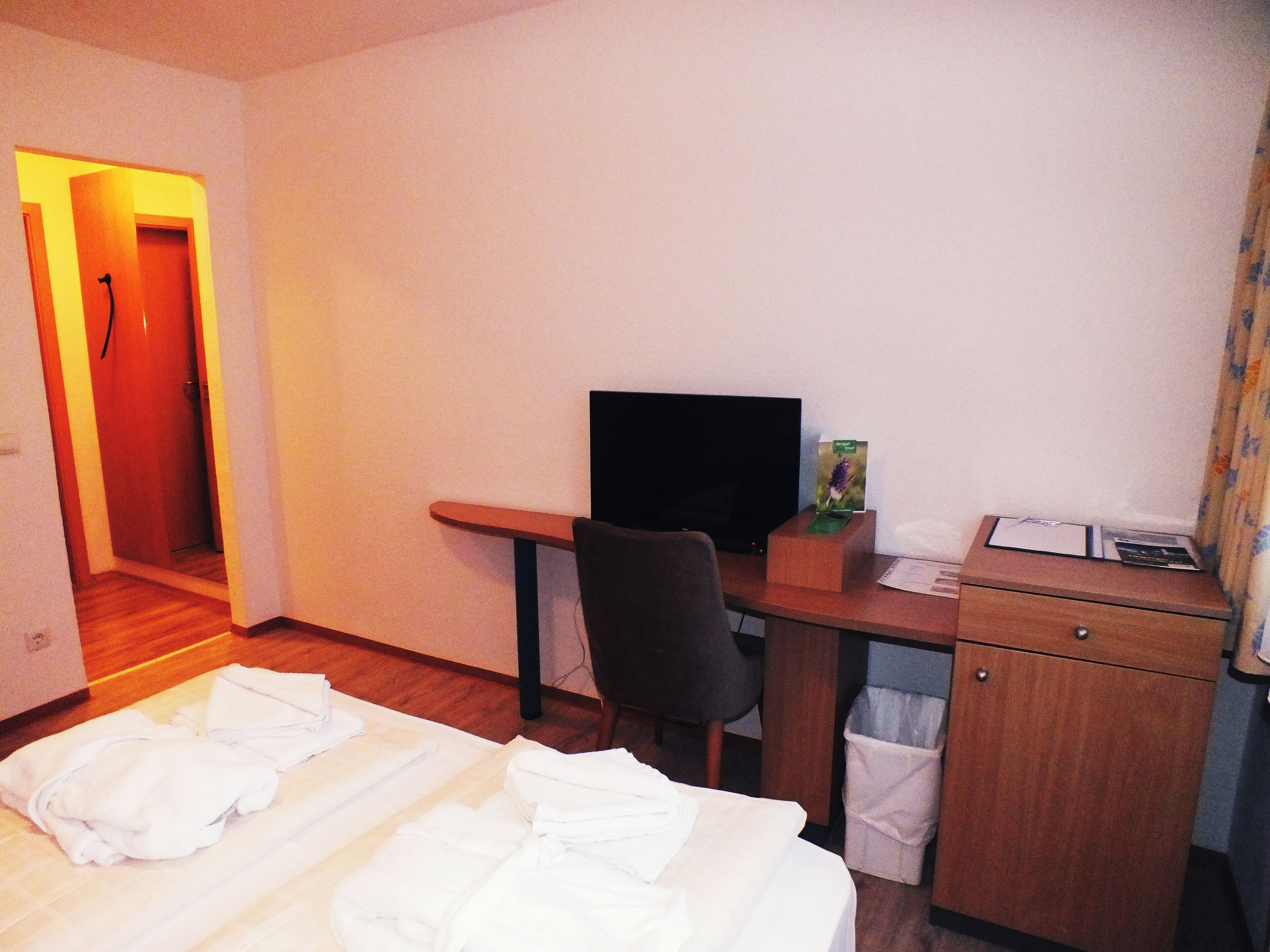 A hotel room with a bed, a desk with a computer, a chair, a TV, and a small cabinet.