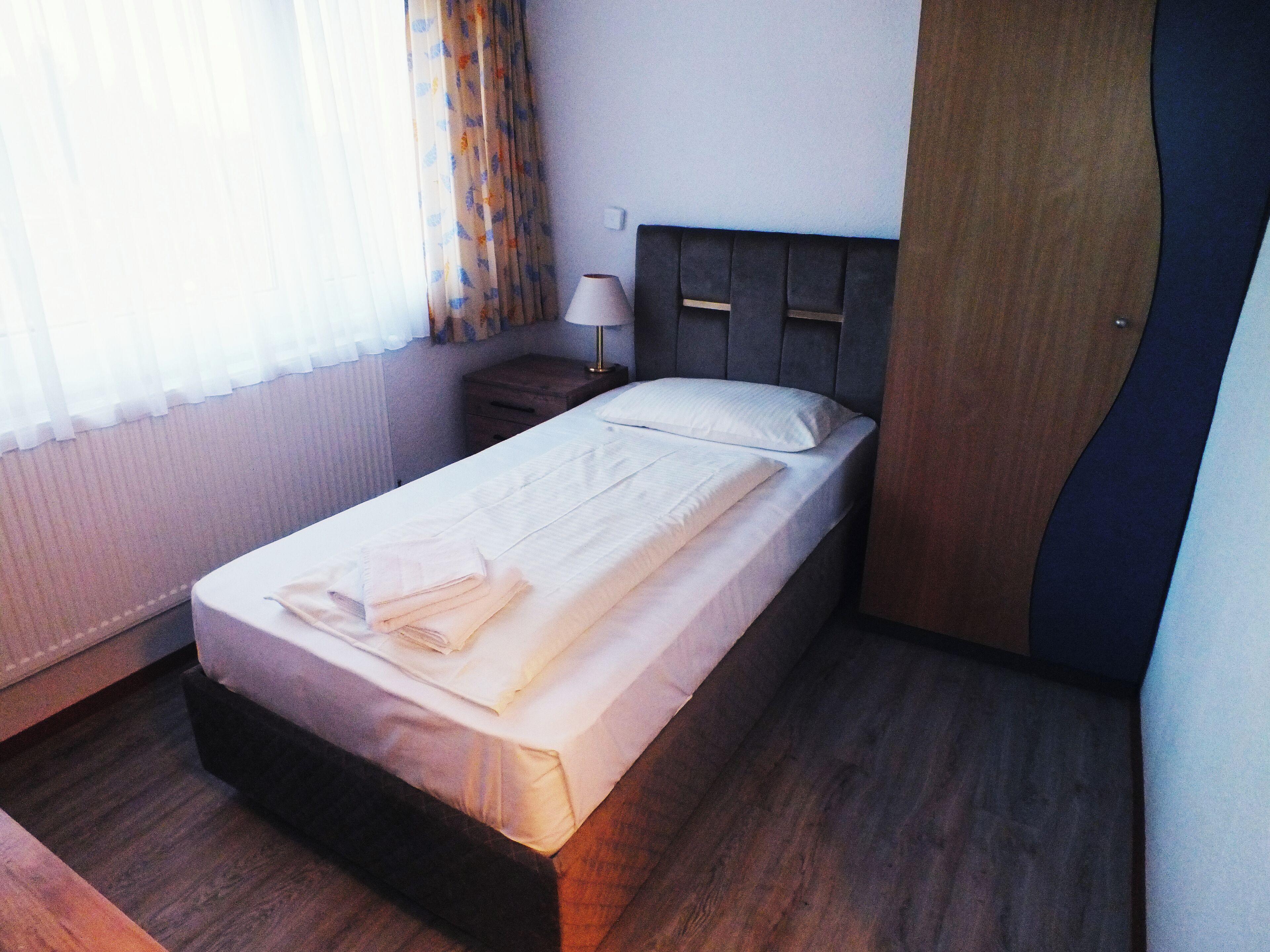 Un lit bien fait, avec une serviette pliée, une lampe de chevet et une tête de lit en bois, dans une chambre d’hôtel.