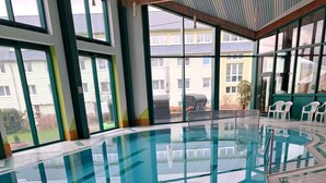 An indoor swimming pool with clear blue tiles, surrounded by a tiled floor and a wooden deck. - Werrapark Hotel Heubacher Höhe (Masserberg)