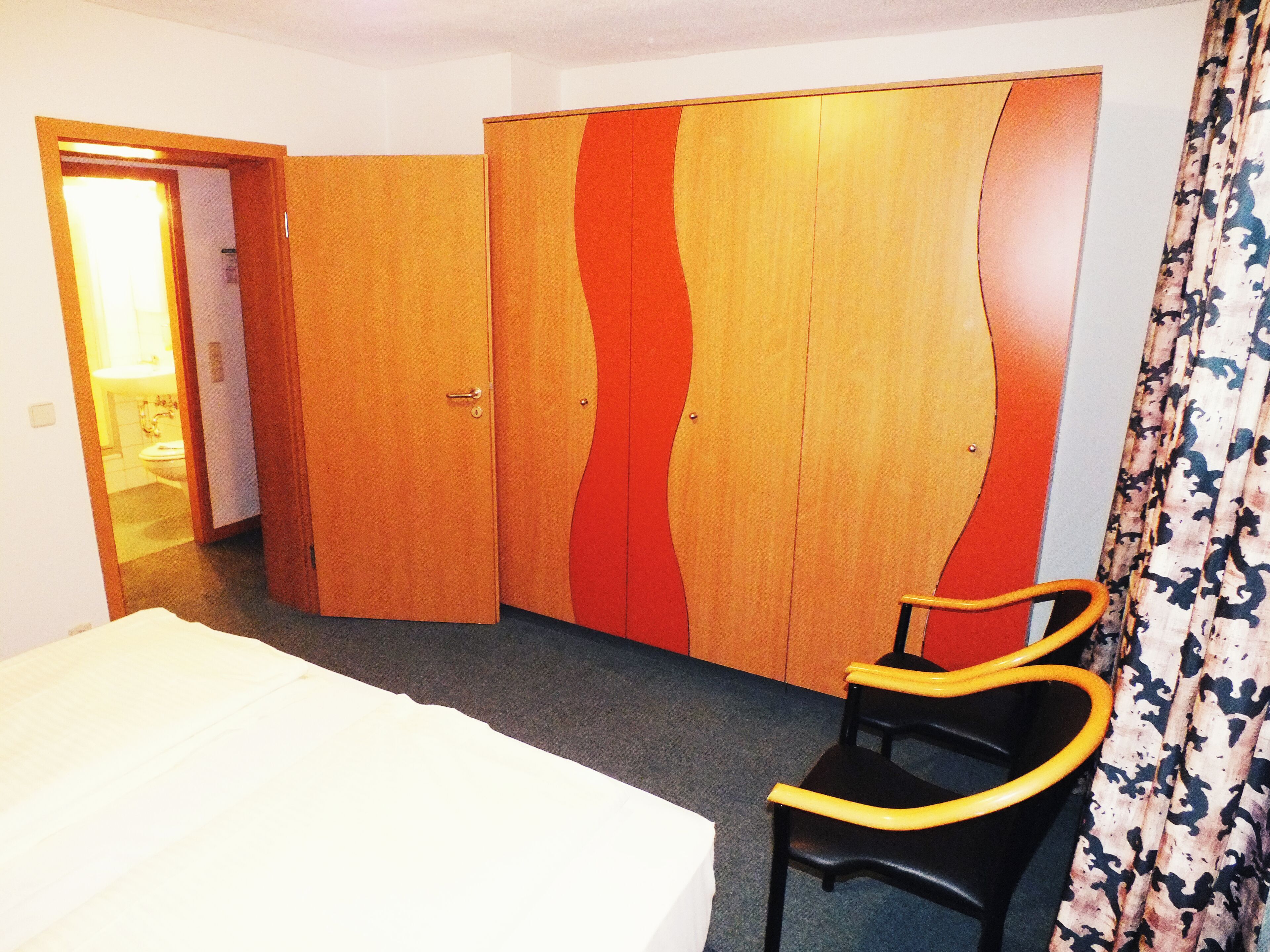 A hotel room with a bed, a chair, and a wardrobe with a unique design.